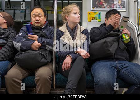 Junge Frau sitzt zwischen zwei großen Männern auf Zug, Tokio, Honshu, Japan Stockfoto