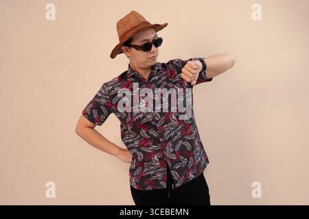 Junger Mann im tropischen Hemd, der seine Uhr überprüft und eine Sonnenbrille trägt Stockfoto
