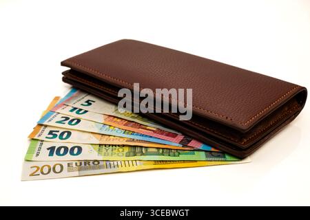 Mehrere Euro-Banknoten Verteilt. Geschlossene braune Ledergeldbörse mit fächerten Euro-Banknoten auf weißem Hintergrund. Stockfoto