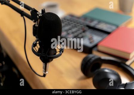 Ein kreativer Arbeitsbereich für Podcast-Aufnahmen mit Mikrofon, Kopfhörern und Schreibtisch, der die Produktion und Kommunikation digitaler Medien symbolisiert. Stockfoto
