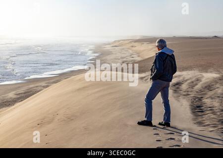 Mann am Rande der Sanddünen mit Blick auf den Atlantischen Ozean - Skeleton Coast National Park, Namibia, Afrika Stockfoto