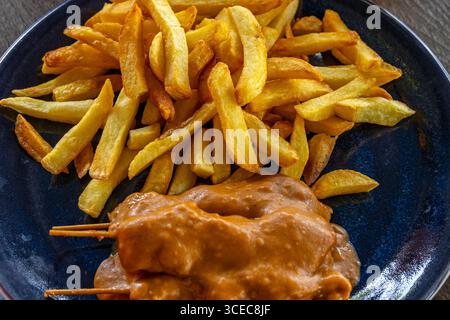Hähnchensaft in Erdnusssauce auf Sticks mit hausgemachten frittierten Pommes frites auf einem Teller mit Blick von oben Stockfoto