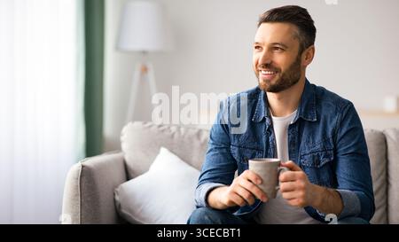 Fröhlicher bärtiger Mann, der zu Hause eine Tasse Kaffee genießt Stockfoto