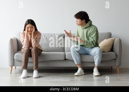 Missverständnisse in Beziehungen. Millennial asiatisches Paar streitete zu Hause auf der Couch, Mann schrie seine Frau an Stockfoto