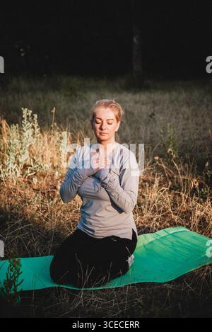 Frau, die Yoga und Meditation über die Natur praktiziert, sitzt in Lotusposition auf Yogamatte, entspannt mit geschlossenen Augen. Achtsames Meditationskonzept. Wohlbefinden. Stockfoto