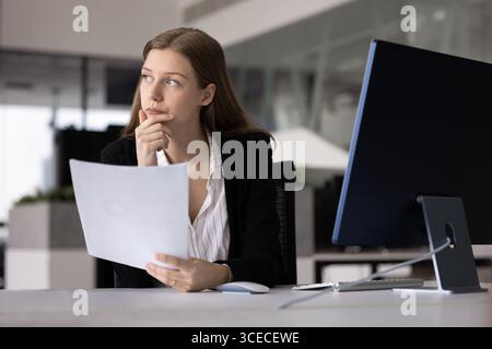 Ernsthafte nachdenkliche junge Geschäftsfrau, die das Kinn berührt und wegschaut Stockfoto