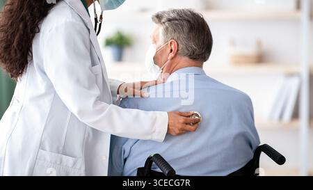 Leitender männlicher Patient im Rollstuhl, der an Atemwegserkrankungen leidet, mit Coronavirus, medizinische Fachkraft, die ihm hilft Stockfoto