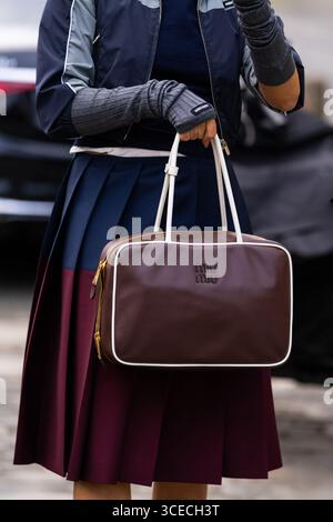 Paris, Frankreich - 11. März 2025: Frau trägt braune Miu Miu-Handtasche mit weißer Paspelierung, zweifarbigem Faltenrock und fingerlosen Logohandschuhen. Street-Style Stockfoto