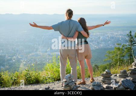 Glückliche junge Reisende Mann und Frau, die sich mit ausgestreckten Armen umarmen und während ihrer Reise vom Aussichtspunkt aus die wunderschöne Stadt bewundern. Stockfoto