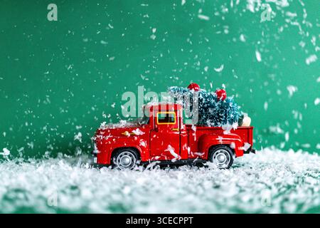 Winterliches Bild eines roten Spielzeugwagens mit einem Miniatur-Weihnachtsbaum, der durch künstlichen Schnee mit einem leuchtend grünen Hintergrund verziert ist. Sturz Stockfoto