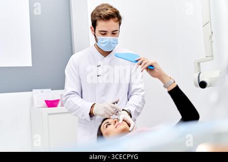 Ein Arzt, der weiße sterile Handschuhe trägt, verabreicht einem Patienten in einer modernen Arztpraxis vorsichtig eine Hyaluronsäure-Injektion, wobei er die Präzisi betont Stockfoto