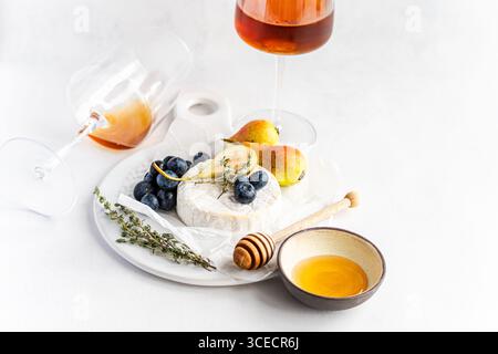 Elegantes Stillleben mit cremigem Brie-Käse, Reifen Heidelbeeren und saftigen Birnen, ergänzt durch Honig, alles begleitet von einem Glas Bernsteinwein Stockfoto