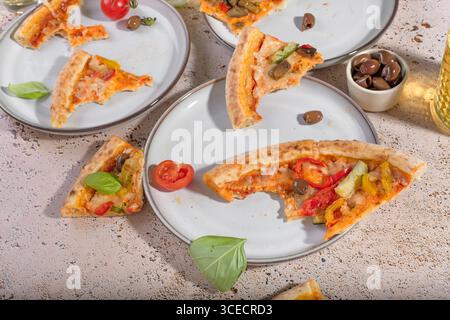 Vegetarische Pizza mit Basilikum, Käse und gemischtem Gemüse stehen einladend auf Tellern. Die Szene fängt eine ungezwungene, köstliche Imbissatmosphäre mit ein Stockfoto