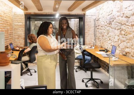 Eine vielfältige Gruppe von Frauen arbeitet in einem trendigen Coworking-Bereich zusammen und nutzt Technologie für produktive Diskussionen. Notebooks und Tablets Stockfoto