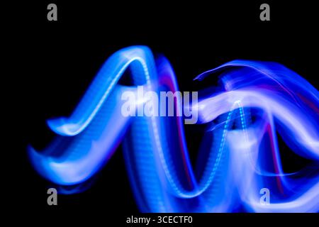 Ein dynamisches abstraktes Bild mit leuchtenden blauen und violetten Lichtspuren, die auf schwarzem Hintergrund schweben und eine energiegeladene und geheimnisvolle Darstellung erzeugen Stockfoto