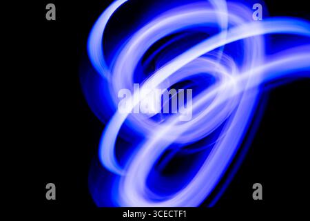 Ein dynamisches abstraktes Bild mit leuchtenden blauen und violetten Lichtspuren, die auf schwarzem Hintergrund schweben und eine energiegeladene und geheimnisvolle Darstellung erzeugen Stockfoto