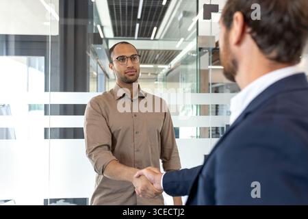 Zwei Profis begrüßen sich mit einem Handschlag in einer modernen Büroumgebung und fördern so die Zusammenarbeit. Stockfoto