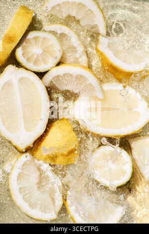 Lebendige Zitronenscheiben sorgen für einen Spritzer in kristallklarem Wasser und zeigen die erfrischende Essenz von Zitrusfrüchten vor einem hellen Hintergrund. Stockfoto