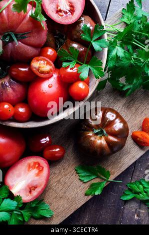 Blick von oben auf verschiedene Tomaten mit frischer Petersilie auf einem rustikalen Holzbrett. Die lebendigen Farben und natürlichen Texturen sorgen für eine frische und gesunde Ernte Stockfoto