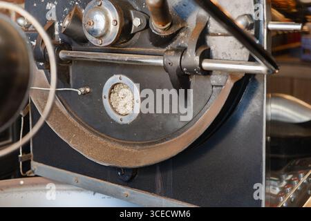 Nahaufnahme einer Kaffeeröstermaschine mit grünen Kaffeebohnen im Inneren. Die industrielle Einrichtung hebt den Röstprozess hervor, der für Spezialprodukte und A von entscheidender Bedeutung ist Stockfoto