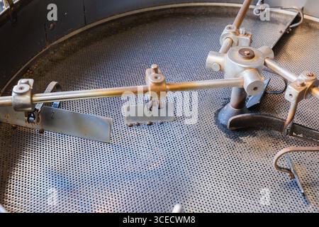 Eine Nahaufnahme einer Kaffeeröstermaschine mit komplizierten rotierenden Schaufeln, die beim Mischen von Kaffeebohnen für ein gleichmäßiges Rösten in einem handwerklich hergestellten Kaffee verwendet werden Stockfoto