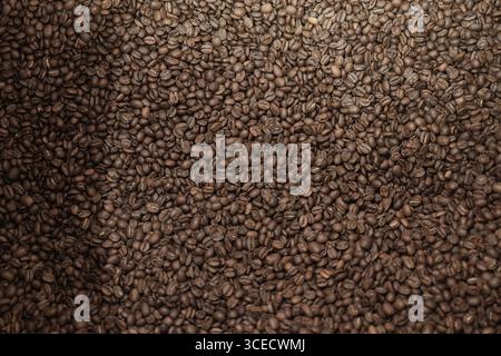 Eine Nahaufnahme eines großen Haufens frisch gerösteter Kaffeebohnen, die ihre satte Farbe und Textur hervorheben. Ideal für handwerkliche Brauereien und Spezialprodukte Stockfoto