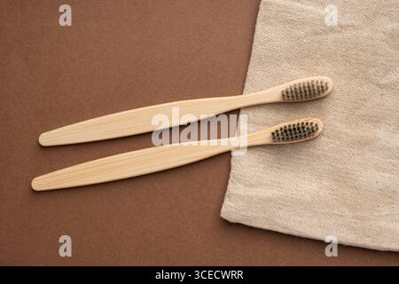 Blick von oben auf zwei Bambus-Zahnbürsten auf brauner Oberfläche, begleitet von naturbeigem Stoff, der umweltfreundliche und nachhaltige Toilettenartikel betont. Stockfoto