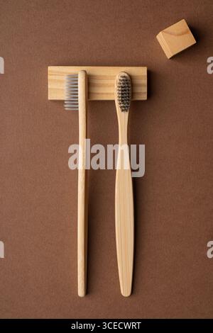 Draufsicht von zwei Bambus-Zahnbürsten auf einer naturbraunen Oberfläche. Holzblock schmückt die Szene und hebt nachhaltige Toilettenartikel hervor Stockfoto
