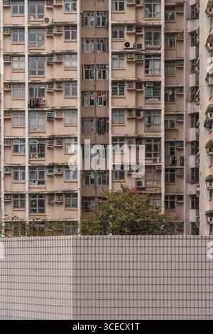 Eine Nahaufnahme eines dicht gepackten Wohngebäudes in Hongkong, das urbanes Leben mit zahlreichen Fenstern, Balkonen und Klimaanlage veranschaulicht Stockfoto