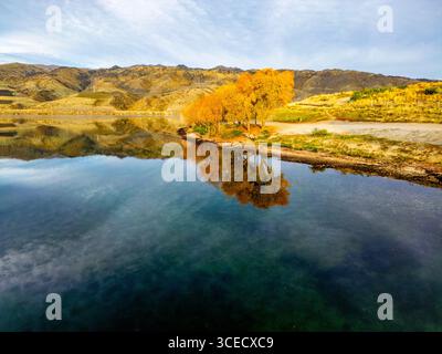 Atemberaubende Herbstfarben rund um einen ruhigen neuseeländischen See in Queenstown aus der Vogelperspektive. Die majestätische Landschaft spiegelt sich im klaren Seenwasser, f Stockfoto
