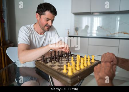 Vater und erwachsener Sohn genießen ein Schachspiel, das die Beziehungen zwischen den Generationen fördert und eine gute Familienzeit in HO verbringt Stockfoto