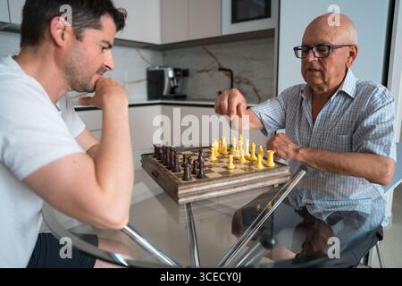 Ein reifer Vater und sein erwachsener Sohn verbringen gute Zeit zu Hause, indem sie Schach spielen. Dieses Bild zeigt eine sinnvolle intergenerationelle Bindungsmutter Stockfoto