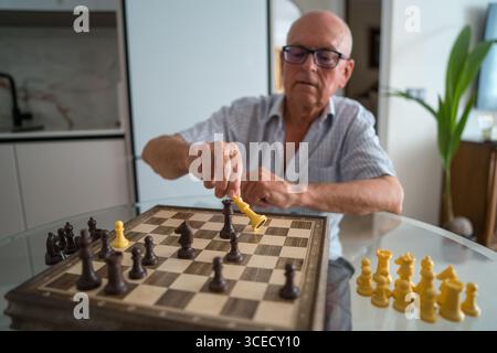 Ein Senior-Mann ist zu Hause intensiv in einem Schachspiel engagiert und konzentriert sich auf seinen nächsten strategischen Schritt. Die entspannte Atmosphäre unterstreicht einen Moment der Freizeit Stockfoto
