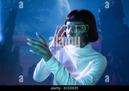 Latin Woman in futuristischer Kleidung erforscht die virtuelle Realität mit fortschrittlichen VR-Brillen, die in eine digitale Landschaft eingetaucht sind. Das Konzept hebt die moderne Technik hervor Stockfoto
