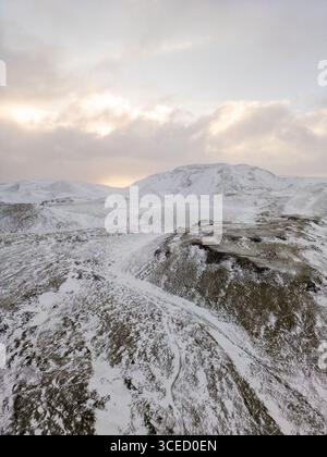 Blick aus der Vogelperspektive auf Islands Winterlandschaft mit schneebedeckten Hügeln und fernen Bergen unter einem sanft beleuchteten Sonnenaufgang, der die abgelegenen und hervorhebt Stockfoto