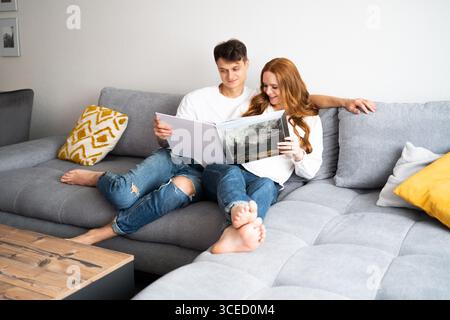 Ein junges Paar sitzt eng auf einem modernen Sofa, vertieft darin, zusammen ein Buch zu lesen. Sie teilen einen friedlichen und intimen Moment, betonen Wärme und Stockfoto