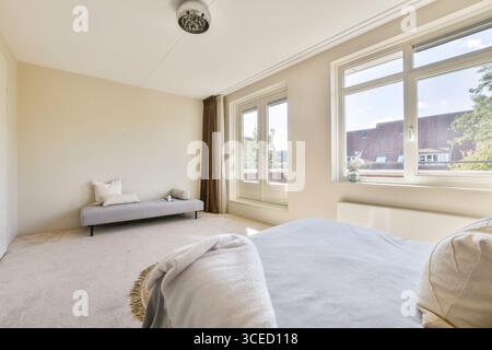 Ein modernes, minimalistisches Schlafzimmer mit gemütlicher, lichtdurchfluteter Atmosphäre. Der Raum ist elegant eingerichtet, mit weichen Teppichen und großen Fenstern für natürliche B Stockfoto