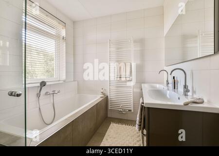 Helles und geräumiges, modernes Badezimmer mit großer Badewanne, zwei eleganten Waschbecken und praktischem Handtuchheizer. Natürliches Licht strömt durch den Wind Stockfoto