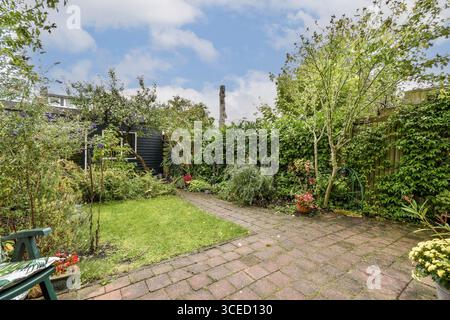 Eine üppige Gartenszene mit einem gepflasterten Weg umgeben von lebendigen Pflanzen und Bäumen. Die ruhige Umgebung ist perfekt zum Entspannen mit einladenden Stockfoto