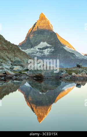 Majestätischer Blick auf das Matterhorn in den Schweizer Alpen, das sich in ruhigem Wasser spiegelt. Der ikonische pyramidenförmige Gipfel steht hoch vor einem klaren blauen Himmel, Show Stockfoto
