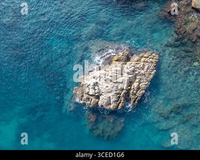 Ein Blick aus der Vogelperspektive fängt einen zerklüfteten Felsvorsprung ein, umgeben von klarem azurblauem Wasser des Mittelmeers, und zeigt die natürliche Schönheit der Costa Blanc Stockfoto