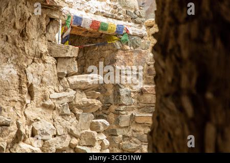 Rustikale Steinmauern, die mit lebhaften Gebetsfahnen verziert sind, erfassen die ruhige Atmosphäre eines traditionellen Gebäudes im Zanskar-Tal, Ladakh, Indien, SH Stockfoto