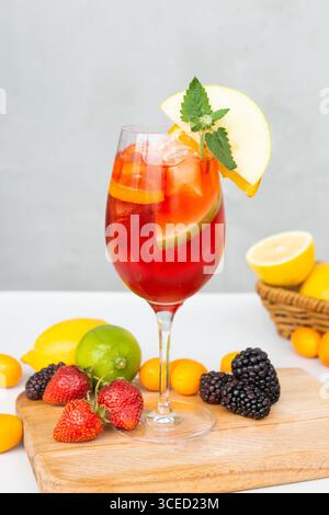 Ein lebhafter Sommercocktail mit Eis und frischen Früchten wie Apfel, Orange und Minze. Umgeben von Zitronen, Limetten, Erdbeeren und Brombeeren Stockfoto