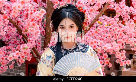 Frau in traditioneller Kleidung der Qing-Dynastie steht inmitten von Kirschblüten in Pingyao, China, und blickt direkt in die Kamera und verkörpert historische Elemente Stockfoto