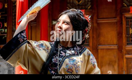 Eine junge Frau in traditioneller Kleidung der Qing-Dynastie posiert mit einem Fan in Pingyao, China. Ihre ausgeklügelte Frisur und Kleidung spiegeln die reiche Scul wider Stockfoto