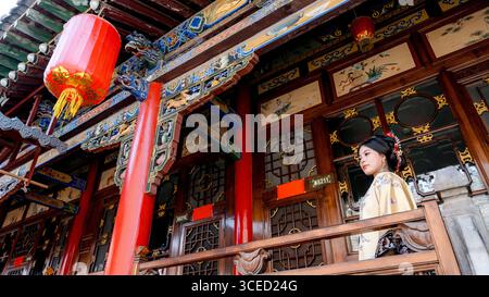 Eine Frau in traditionellem Kostüm der Qing-Dynastie steht anmutig auf einem Holzbalkon in Pingyao, China, umgeben von aufwendig geschnitzten Architekten Stockfoto