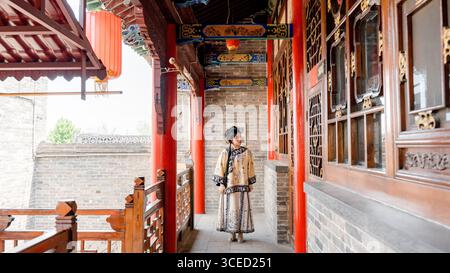 Eine junge Frau in traditioneller Kleidung der Qing-Dynastie steht anmutig in einem historischen Korridor in Pingyao, China. Die Umgebung hebt komplizierte Elemente hervor Stockfoto