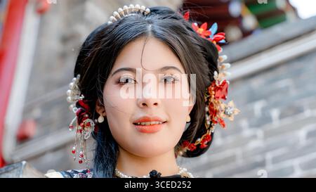 Eine Frau in traditioneller Kleidung der Qing-Dynastie schaut in die Kamera in Pingyao, China. Ihr raffinierter Kopfschmuck und ihr kunstvolles Outfit spiegeln historische Elemente wider Stockfoto