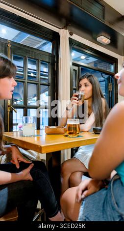 Drei Freunde versammeln sich an einem Holztisch in einem gemütlichen Restaurant, genießen erfrischende Getränke und anregende Gespräche. Die helle Atmosphäre sorgt für Wärme Stockfoto