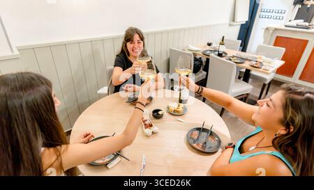 Eine Gruppe von Freunden, die fröhlich mit Weingläsern um einen Tisch toasten, eine köstliche Mahlzeit in einem gemütlichen Restaurant genießen und das wesentliche festhalten Stockfoto